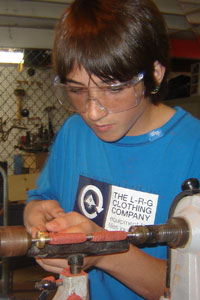 Boy in woodshop working on a lathe.