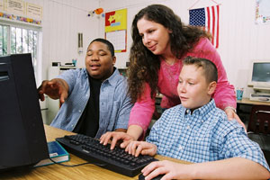 Two boys with female teacher looking at computer.